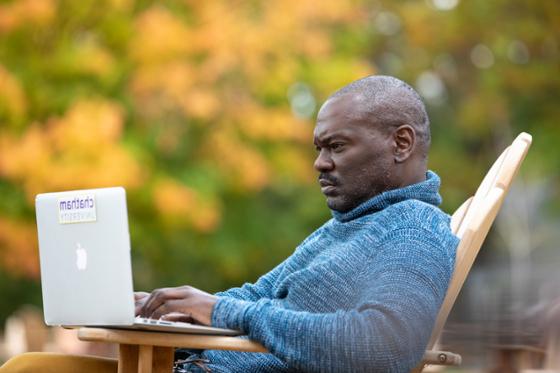 图为一名足球外围买球靠谱的男学生在外面用笔记本电脑工作, with autumnal leaves in the background.