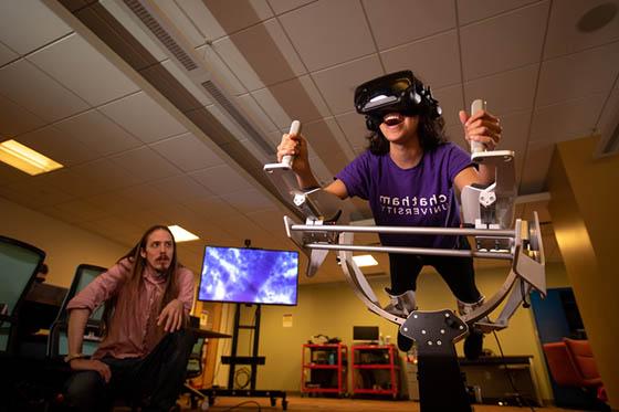 图为一名足球外围买球靠谱的学生在沉浸式媒体实验室的虚拟现实机器里, while a professor watches